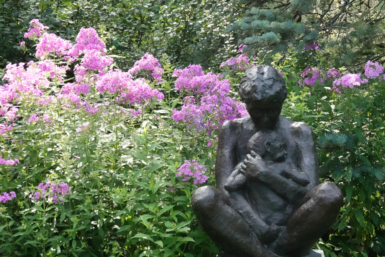 Statue of a mother and child in front of some pink flowers