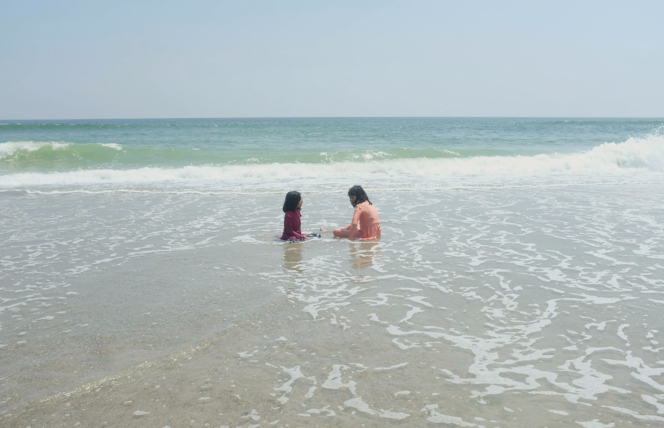 Shot of two girls sitting in the water at the baech