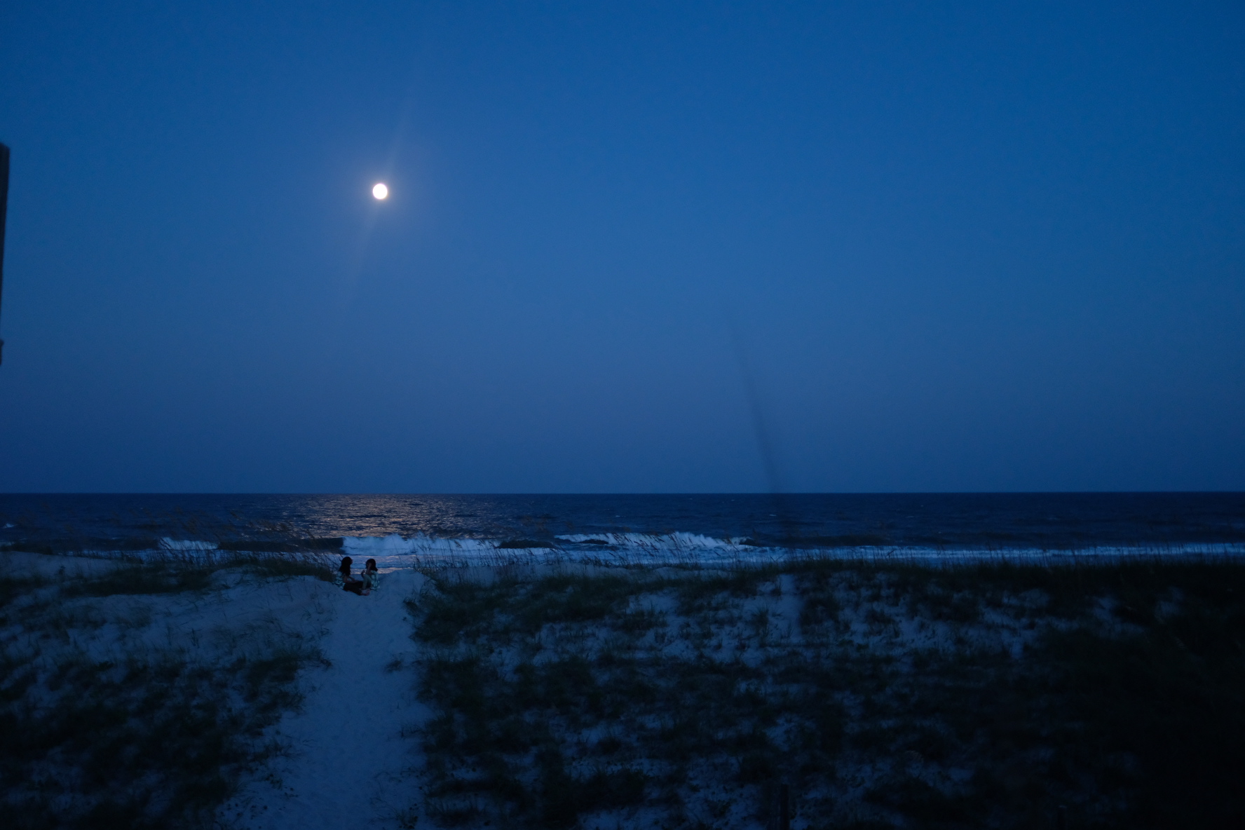 Shot of two girls sitting on the beach under the moonlight