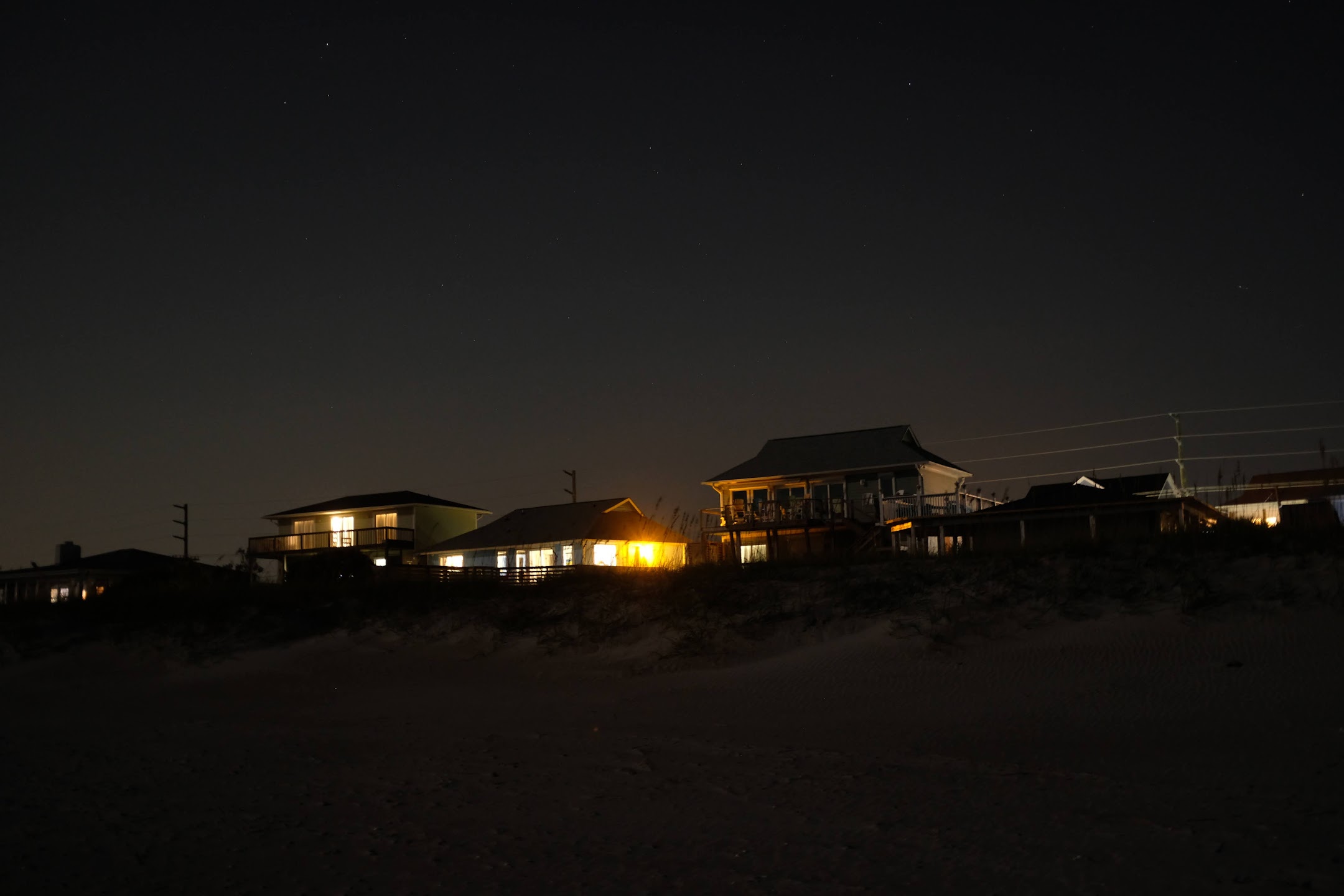 Illuminated houses on Topsail Beach at night, with stars in the sky